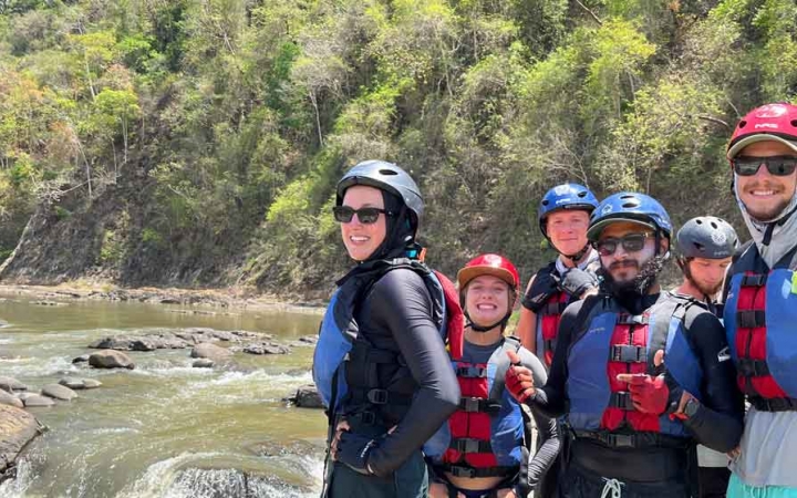 a group of gap year students wear whitewater gear and stand on the edge of a river